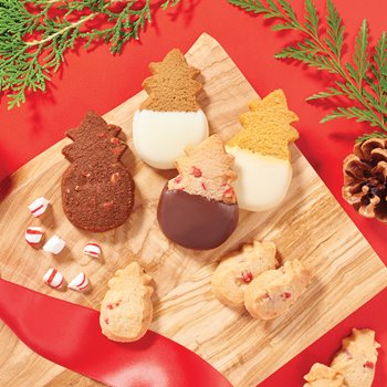 1 chocolate, 3 chocolate-dipped shortbread, & 3 mini shortbread cookies all shaped like pineapples sitting on a wooden board next to chunks of peppermint.