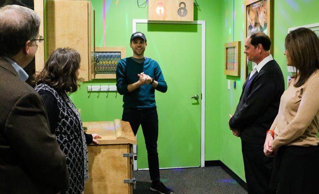 Male Breakout Waikiki employee speaking to a group of people in business attire at the entrance of an escape room.
