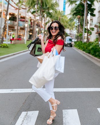 Woman wearing sunglasses crossing the street while holding many shopping bags.