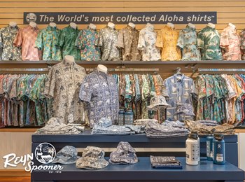 Display of colorful aloha shirts and accessories on shelves in a reyn spooner store with a sign stating "the world's most collected aloha shirts".