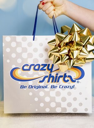 Hand holding a white & gray Crazy Shirts shopping bag with a gold bow on it.