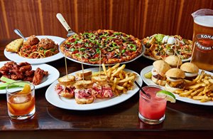 Spread of burgers, pastrami sandwiches, chicken wings, pasta, pizza, beer & cocktails