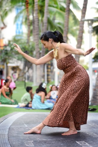 Female hula dancer looking down at one foot extended out in front of her body