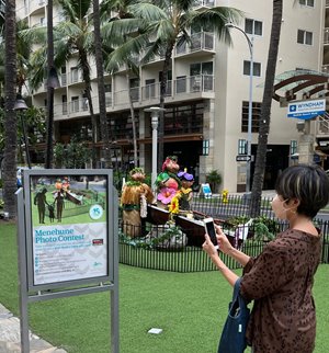 Woman taking a picture of the menehune installation for a photo contest.