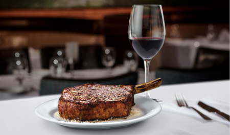 Bone-in cowboy ribeye steak plated next to a glass of red wine on a table at Ruth's Chris Steak House in Waikiki.
