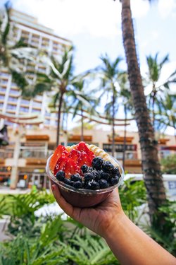 Hand holding a bowl of acai topped with bananas, strawberries, & blueberries.