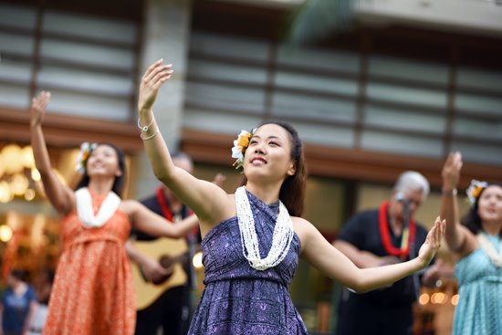 Hula dancer wearing a purple dress, mid-dance with her hand up in the air