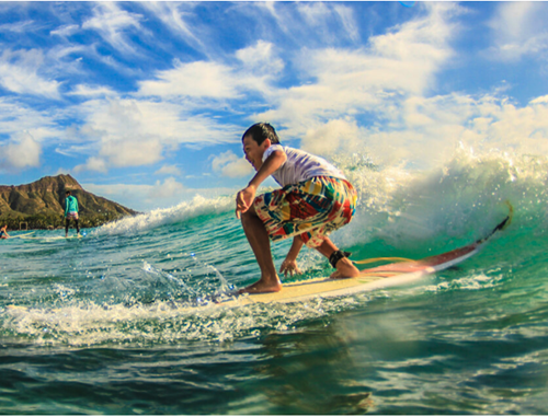 Young boy in colorful board shorts surfing a wave with Diamond Head in the background