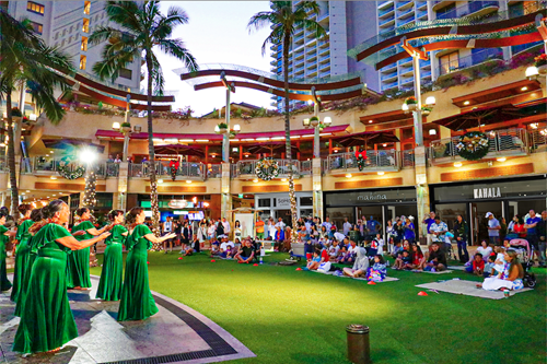 Holiday hula performance in front of a crowd on Waikiki Beach Walk's lawn.