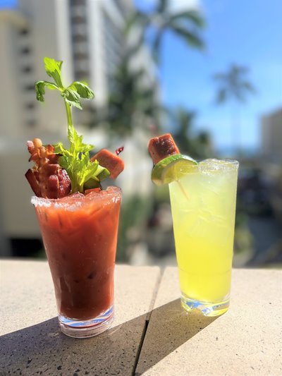 Fully garnished Bloody Mary on the left & yellow cocktail with a SPAM cube garnish on the right.