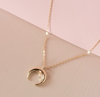 Gold chain necklace with a crescent moon pendent on a blush pink table