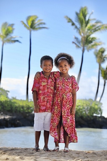 Two young children wearing matching red aloha attire while standing on a beach in Hawaii