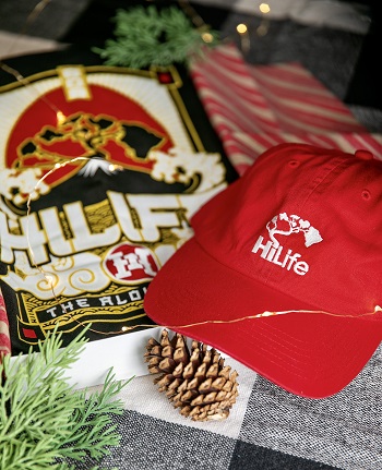 Red HiLife cap with tree logo & a HiLife shirt with the tree logo on above a mountain with a red sun in the background.