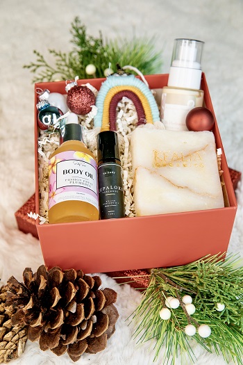 Body oil, soap, & sprays in a red box with Christmas decorations around it.