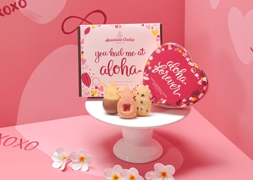 Honolulu Cookie Company's Valentine's Collection featuring a heart-shaped tin that says "aloha forever" and a box saying "you had me at aloha" on a display with 3 pineapple-shaped cookies.