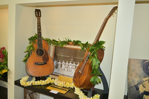 2 guitars propped up on either side of a photo of the string ensemble of the Royal Hawaiian Band in 1934.