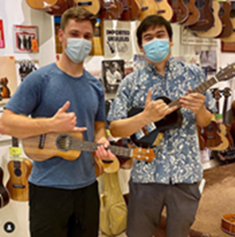 Two men holding ukuleles & flashing a shaka with their hands