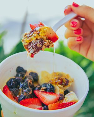 Spoonful of acai & fruit being held over the rest of the acai bowl