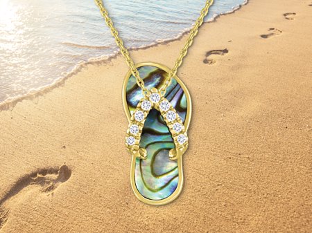 Single slipper with diamond straps & abalone body in front of a beach with footprints in the sand.