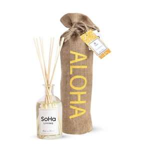 Clear oiil diffuser vessel with a SoHa Living label and reeds sticking out next to a brown burlap bag that says ALOHA