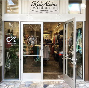 Store front shot of KaiAloha Supply at Waikiki Beach Walk. One of the two doors is open, revealing racks of clothes