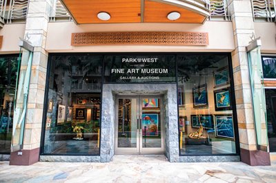 Store front shot of Park West Fine Art Museum & Gallery at Waikiki Beach Walk. Various paintings are visible through the glass doors and window.