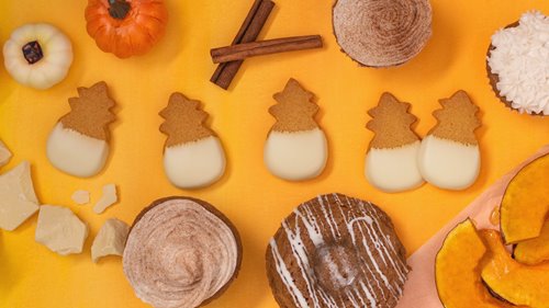 5 pineapple-shaped, white chocolate dipped cookies on an orange backdrop surrounded by mini pumpkins, cinnamon sticks, cinnamon powder cupcakes, etc.