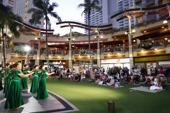 Hula group in green dresses performing for a crowd on the lawn at Waikiki Beach Walk