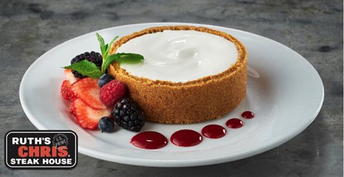Round cheese cake with crust all around next to berries on a white plate