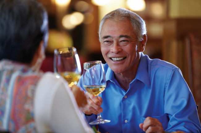 Older gentleman holding a glass of white wine while sitting across of a woman in Roy’s Waikiki.