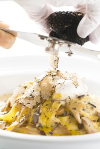 Black truffle being shaved over a bowl of carbonara with a poached egg on top.