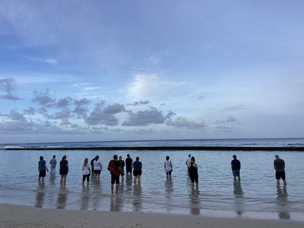 Group of people standing knee deep in the ocean in the morning.
