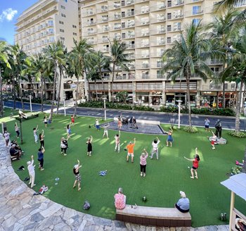 a grass lawn in front of a building with people dancing hula on the lawn