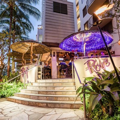Roy's Waikiki exterior shot of the stairs leading up to the entrance. There are two umbrellas on either side of the entrance with string lights and a sign on the right wall that says "Roy's."