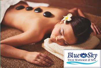 A woman relaxes on a massage table with hot stones placed on her back.